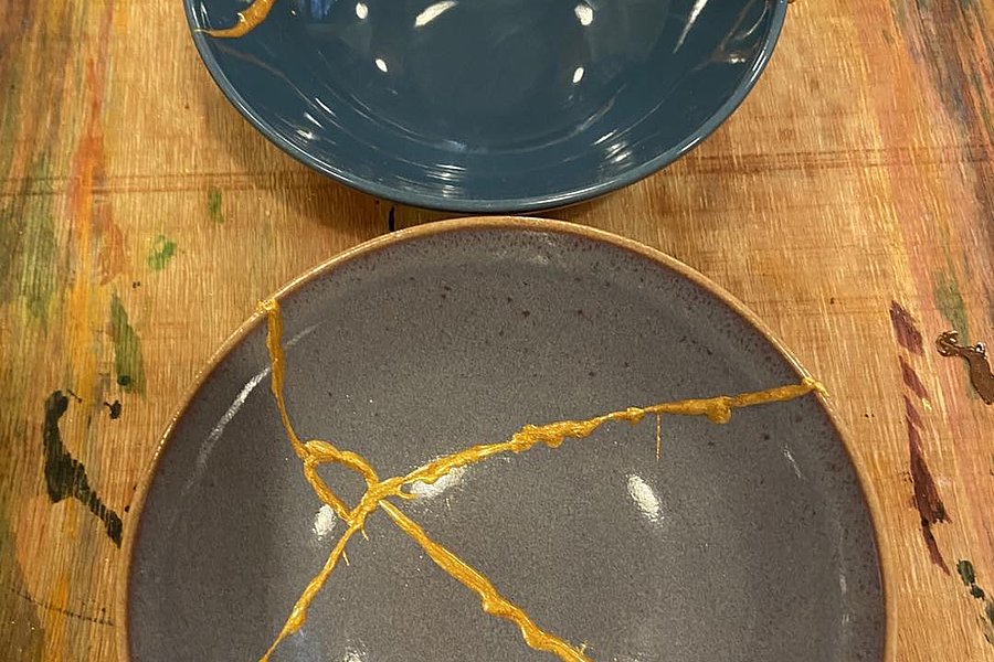 Zwei Keramikschalen, eine dunkelblau und eine grau, mit goldfarbenen Reparaturlinien auf einem Holzuntergrund.