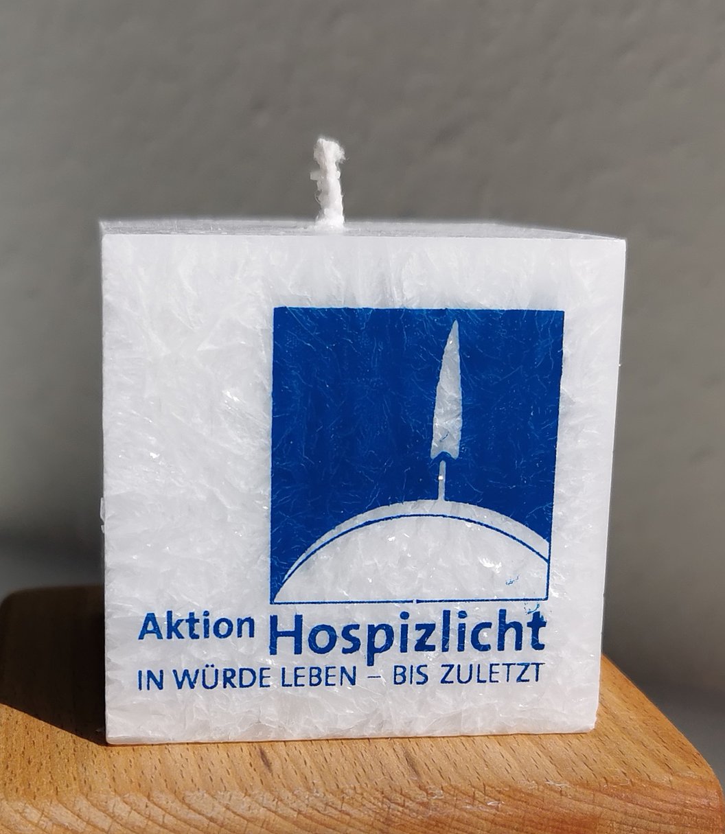 Weiße Kerze mit Logo der Aktion Hospizlicht und dem Slogan „In Würde leben – bis zuletzt“.