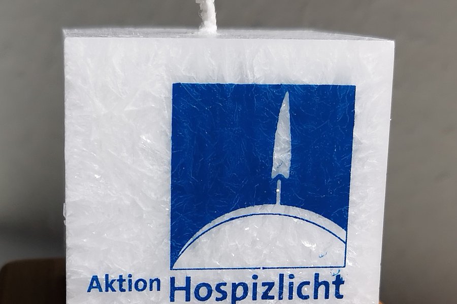 Weiße Kerze mit Logo der Aktion Hospizlicht und dem Slogan „In Würde leben – bis zuletzt“.