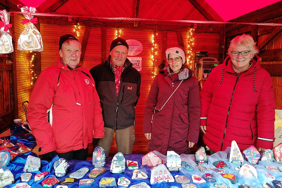 Vier Personen in roten Jacken stehen hinter einem Marktstand mit vielen bunt bemalten Steinen und kleinen Figuren.