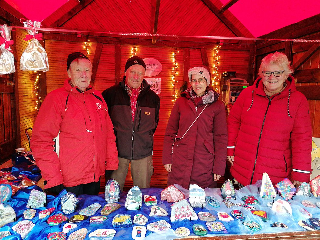 Vier Personen in roten Jacken stehen hinter einem Marktstand mit vielen bunt bemalten Steinen und kleinen Figuren.