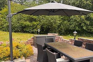 Gartenbereich mit rechteckigem Tisch, mehreren Stühlen aus Rattan und großem Sonnenschirm