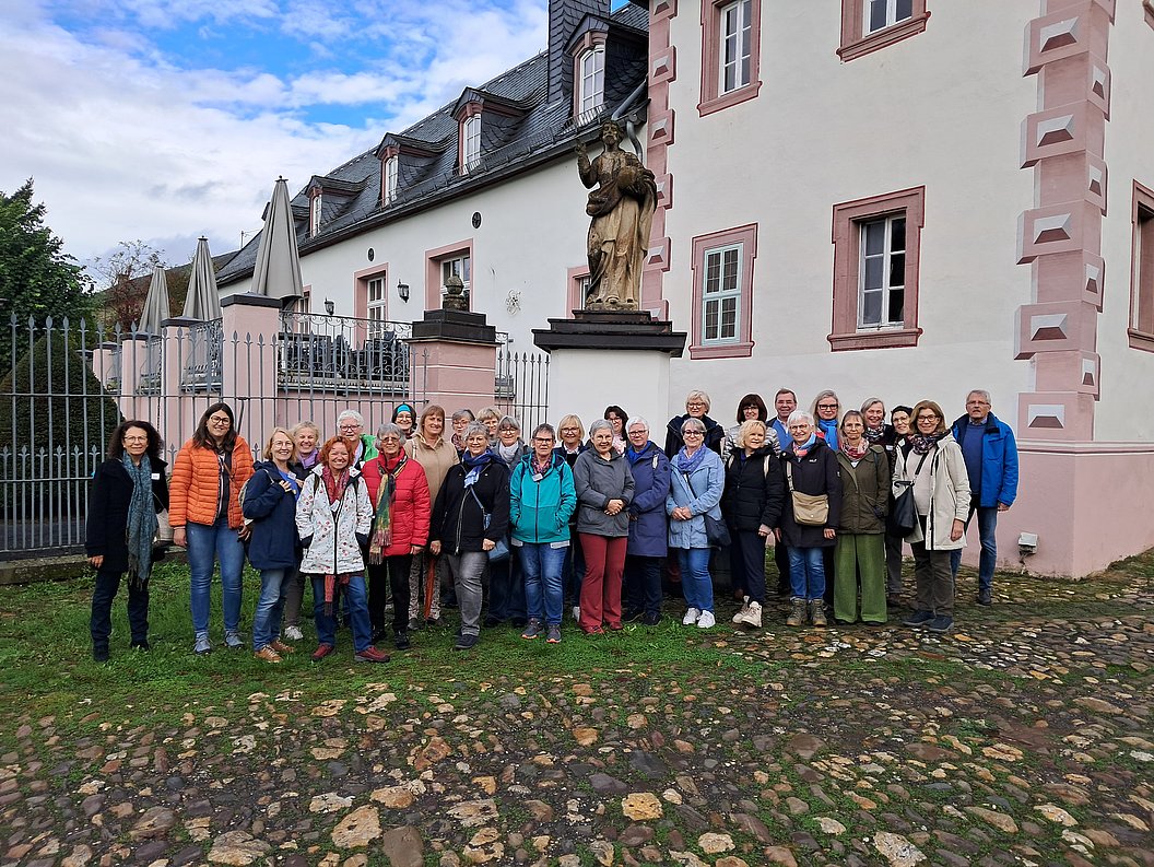 Gruppe von Menschen vor einem historischen Gebäude mit rosa-weißen Fassadenelementen und einer Statue auf einem Sockel im Hintergrund.