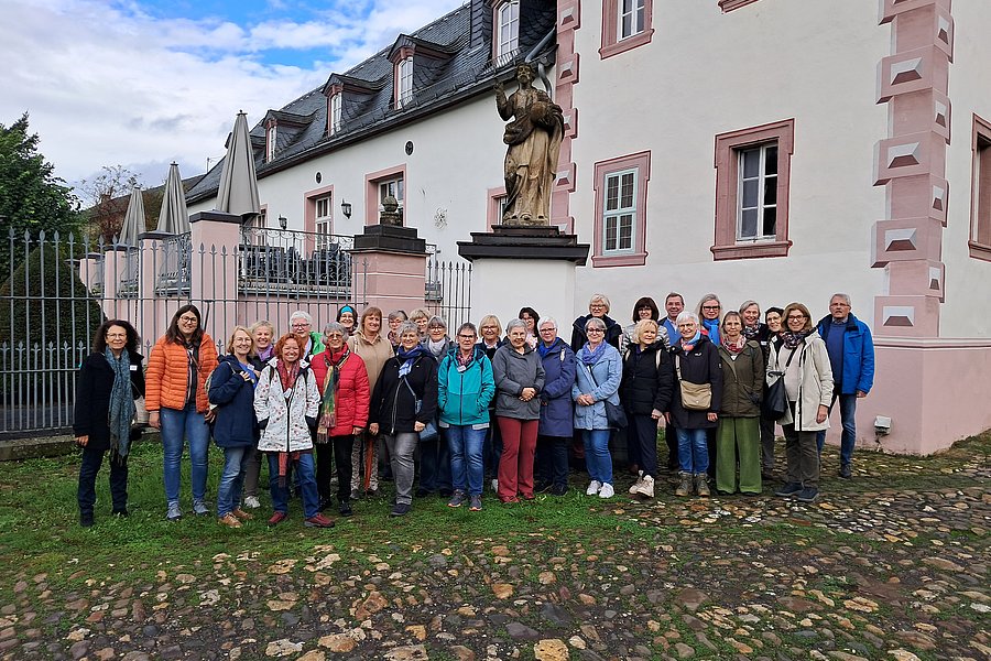 Gruppe von Menschen vor einem historischen Gebäude mit rosa-weißen Fassadenelementen und einer Statue auf einem Sockel im Hintergrund.