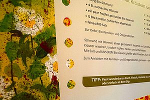 Ausschnitt eines Rezepttextes mit Zutatenliste und Tipp auf weißem Hintergrund neben einer bunten, abstrakten Farbmalerei mit grünen, gelben und roten Farbflecken