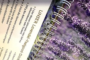 Nahaufnahme eines Spiralbuchs mit lila Lavendelblüten auf der rechten Seite und Text zu einem Lavendel-Feelgood-Drink auf der linken Seite.