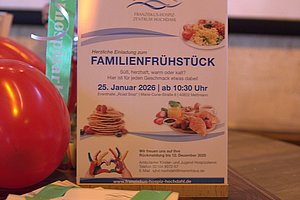 Einladungsflyer zum Familienfrühstück mit Datum und Menüangaben, dekoriert mit Luftballons und Bändern.