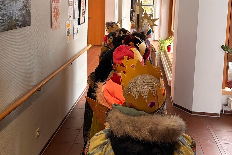 Kinder mit selbstgebastelten Kronen stehen in einem Flur hintereinander