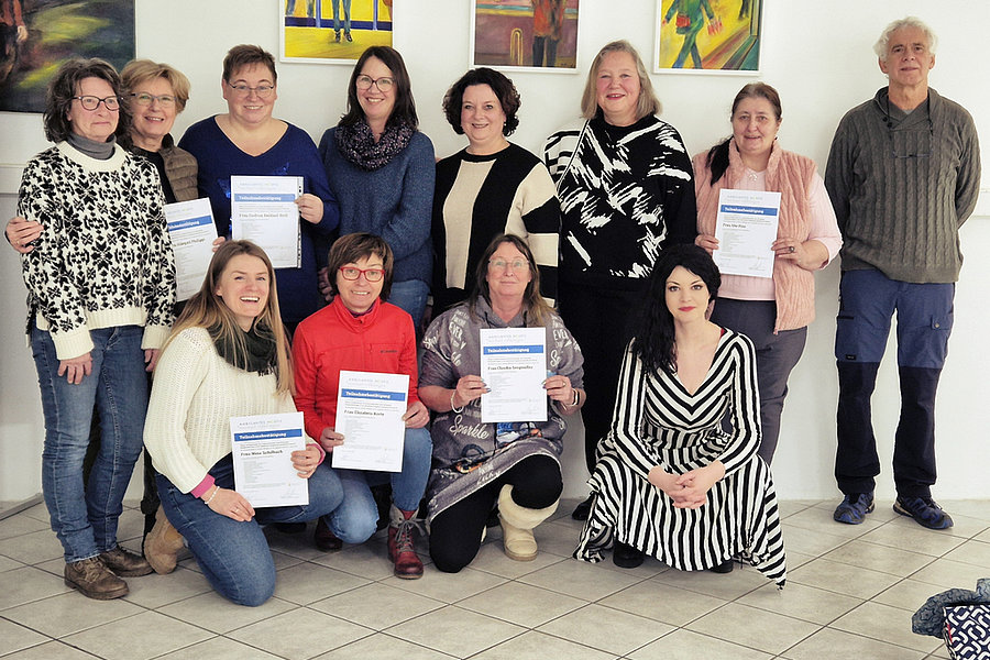 Gruppe von zwölf Personen, einige halten Zertifikate, im Raum mit bunten Gemälden an der Wand.
