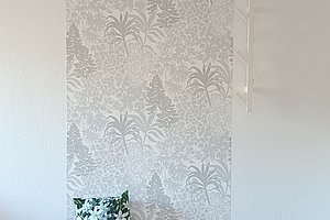 Sessel mit weißem Überwurf und floral gemustertem Kissen vor einer Wand mit floralem Tapetenmuster.