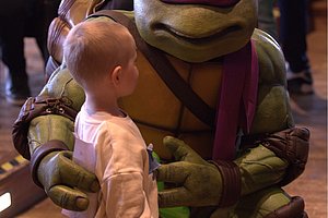 Ein Kind steht vor einem Maskottchen der Teenage Mutant Ninja Turtles, das in einem lebensechten Kostüm auftritt.