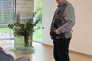 Mann steht vor einer Leinwand in einem Raum mit großen Fenstern und einem Banner des Ambulanten Hospizdienstes