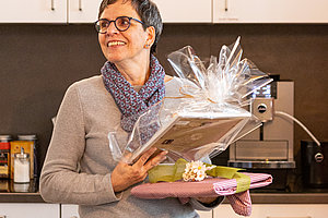 Person steht in einer Küche und hält ein Geschenkpaket mit Geschenkfolie und eine pinke Servierplatte mit Macarons.