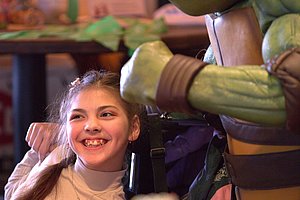 Mädchen lächelt neben einem großen Ninja Turtles Charakter in einem Restaurant.