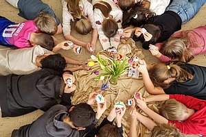 Kinder liegen im Kreis auf dem Boden und halten bemalte Steine in den Händen