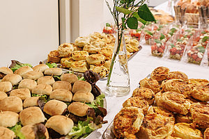 Buffet mit verschiedenen Fingerfood-Snacks, Brötchen, Schalen und einer Rose als Dekoration.