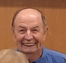 Norbert Becker mit blauer Hemdbluse vor braunem Hintergrund